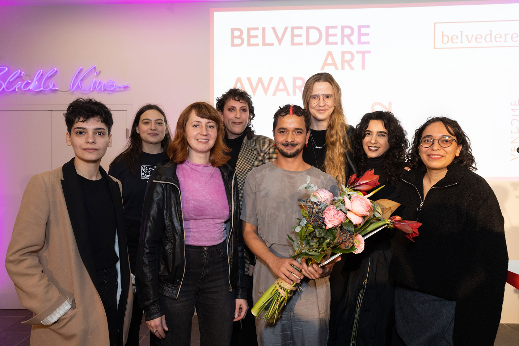 Die nominierten Künstler*innen, Rawan Almukhtar, Robert Gabris, Sophie Gogl, Julia S. Goodman, Claudia Lomoschitz, Pouran Parvizi, Marlies Pöschl, Huda Takriti und Sophie Thun lächeln in die Kamera. Der Preisträger Robert Gabris hält einen Blumenstrauß in der Hand.